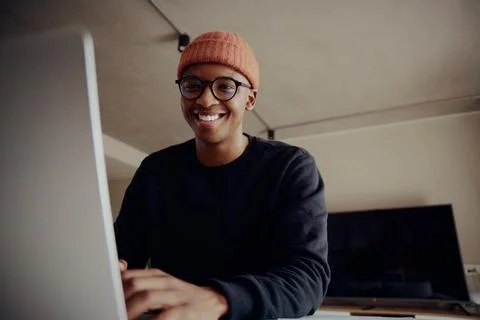 Black male smiling at camera while on laptop sitting at kitchen counter. Young Stock Photos
