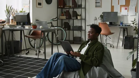 Black Male Software Engineer Sitting Down in Bean Chair to Work with AI Agent Stock Footage 335939611