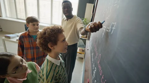 Black Male Teacher Explaining Math on Blackboard to Elementary Students Stock Footage 340548219
