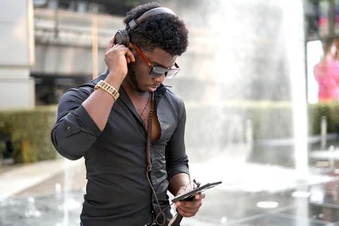 Black man adjusting the headphones while listening to music outdoors Stock Photos