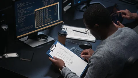 Black Man Analyzing Documents and Coding at Computer in Dark Office Stock Footage 324025954