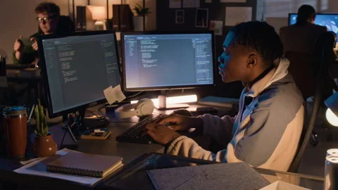 Black Man Coding on Dual Monitors in Office at Night 스톡 동영상 336710542