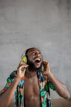 Black man dancing while listening to music in headphones against gray background Stock Photos