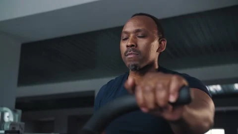 Black man doing cardio workout sitting on bicycle machine in crossfit gym Stock Footage 225715925