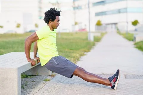 Black man doing triceps dip exercise on city street bench. Fotos de archivo