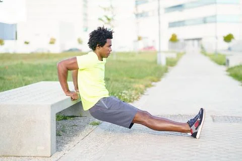 Black man doing triceps dip exercise on city street bench. Stock-Fotos