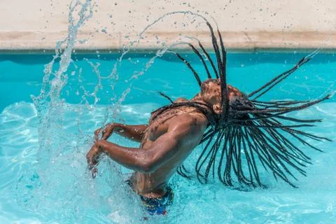Black man with dreadlocks inside a pool raising his wet hair. Stock Photos