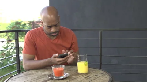 A black man drinks juice and uses his cell phone. Stock Footage 44217982