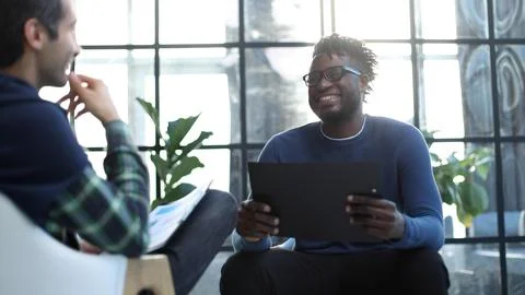 Black man with a folder in his hands laughs while sitting Stock Photos