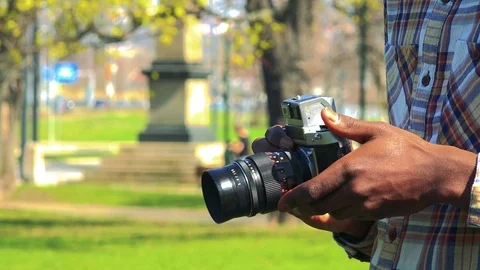 A black man holds a camera in his hands in a park on a sunny day - closeup 库存影片 78432156