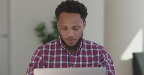 Black man at home using laptop computer remote work talking to co-worker Video stock 169376164