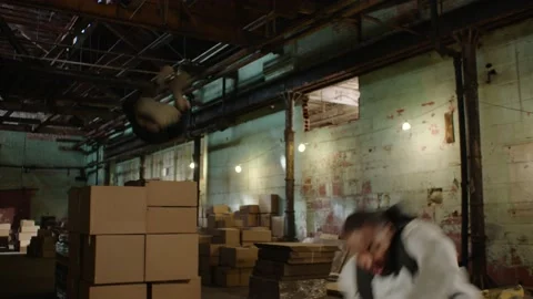 Black man jumps over stack of boxes and is chased by white man in dirty warehous Video stock 199452944