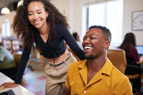 A Black man laughs while his coworker looks over his shoulder at his screen Stock Photos