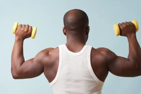 Black man lifting up two light dumbbells from behind. pale blue background Stock Photos