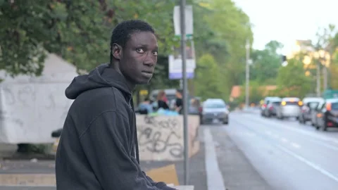 Black man looking away contemplating sitting on a low wall Stock Footage 217818519