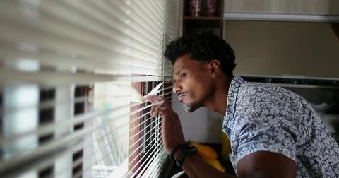 Black man looking through kitchen blinders looking outside Stock Photos