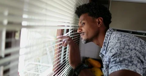Black man looking through kitchen blinders looking outside Stock Photos