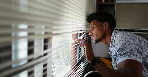 Black man looking through kitchen blinders looking outside Stock Photos