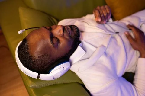 A black man is lying on the sofa and listening to music. A man in a white sui Stock Photos