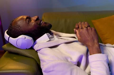 A black man is lying on the sofa and listening to music. A man in a white s.. Foto stock