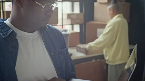 Black Man Managing E-commerce Inventory on Laptop in Warehouse Stock Footage 337310479
