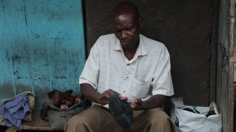 Black man manually repairs shoes, very poor African slums shoe shiner profession Stock Footage 211420606