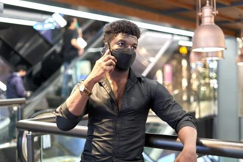 Black man in mask talking to the mobile in a shopping mall Stock Photos