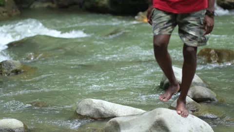 A Black Man Moving From a Boulder to Another Barefoot at a River Stock Footage 207665031