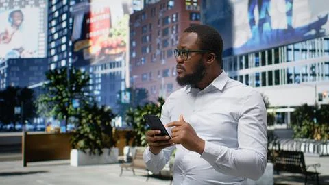 Black man navigating on mobile phone apps and walking busy metropolitan street Stock Photos