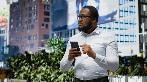 Black man navigating on mobile phone apps and walking busy metropolitan street Stock Photos