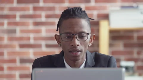 Black man office worker with dreadlocks, glasses and a suit stares intently at Stock Footage 157379397