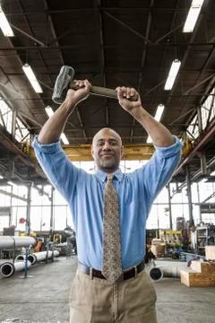 Black man owner of a sheet metal factory holding a hammer while standing on the Stock Photos
