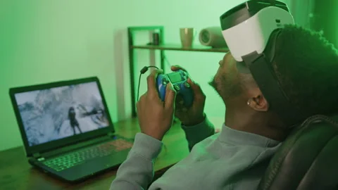 Black man paying on computer using VR headset and game pad Stockbeeldmateriaal 171578981