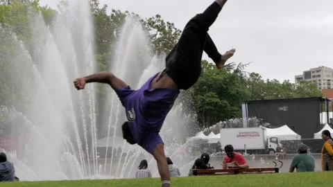 Black Man Performs Martial Arts Tricking On Grass with Fountain, Slow Motion Stock Footage 146552377