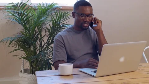Black man on phone call while working on laptop computer Stock Footage 77509745