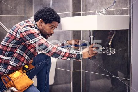 Photograph: Black man, plumber and maintenance in bathroom, fixing sink ...