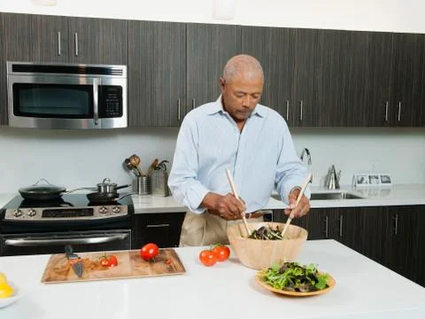 Black man preparing salad in kitchen Stock Photos