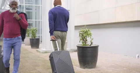 Black man pulling suitcase, glancing at older man rolling luggage in glass Stock Footage 339557507