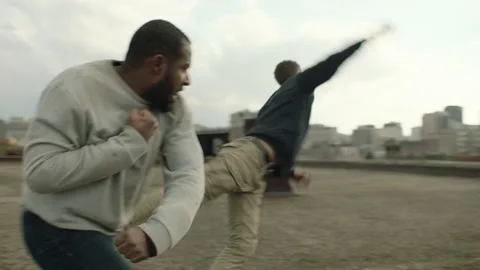 Black man punches and knocks down a white man on a warehouse rooftop in overcast Stock Footage 199459188