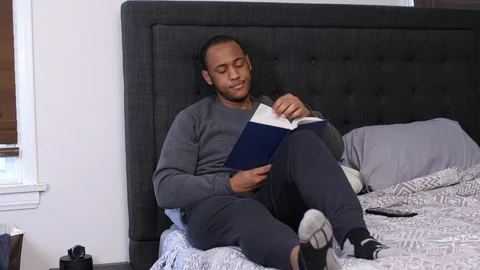 Black man putting down book to look at cell phone Stock Footage 128832790