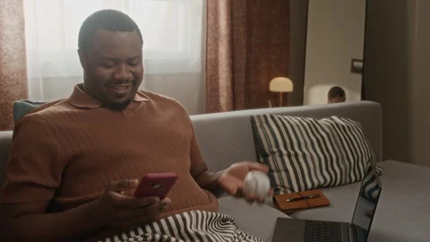 Black Man Relaxing at Home Using Smartphone Tossing Baseball Stock Footage 337717660