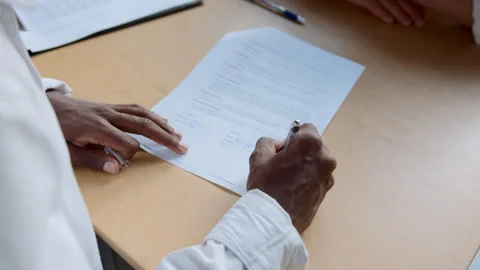 A black man sits at an office desk. He is focused on signing a contract with a 스톡 동영상 335733265