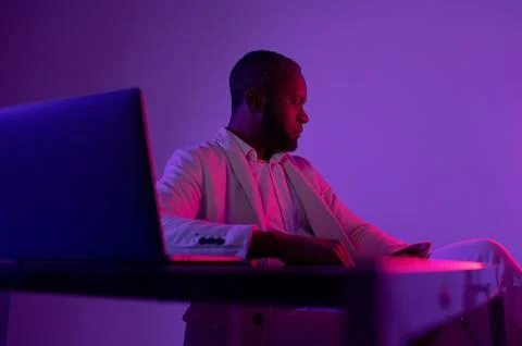 Black man sitting at the computer in the evening office. IT worker in the e.. Foto stock