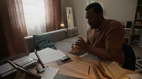 Black Man Sitting at Desk Writing in Notebook Working from Home Stock Footage 338337561