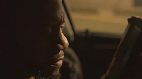 A black man sitting in the driver seat of a car examines his hand gun and Stock Footage 257651244