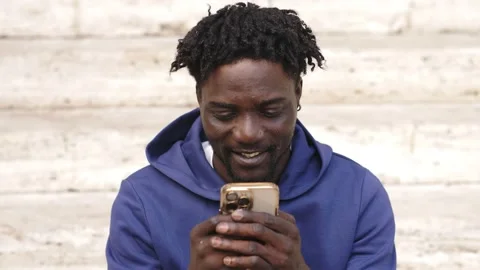Black man sitting on the steps texting on mobile phone  Stock Footage 218602111