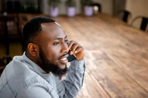 Black man sitting at table having phone call looking away Stock Photos