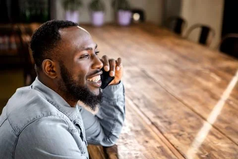 Black man sitting at table having phone call looking away Stock Photos