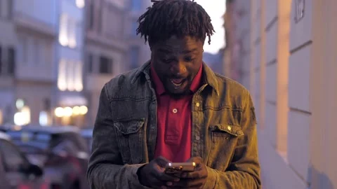 Black man sitting texting on mobile phone on the street Stock Footage 220719136