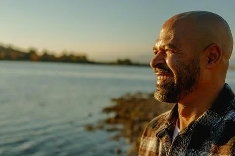 Black man smiling looking at the warm sunset with lake blurred in background Stock Photos